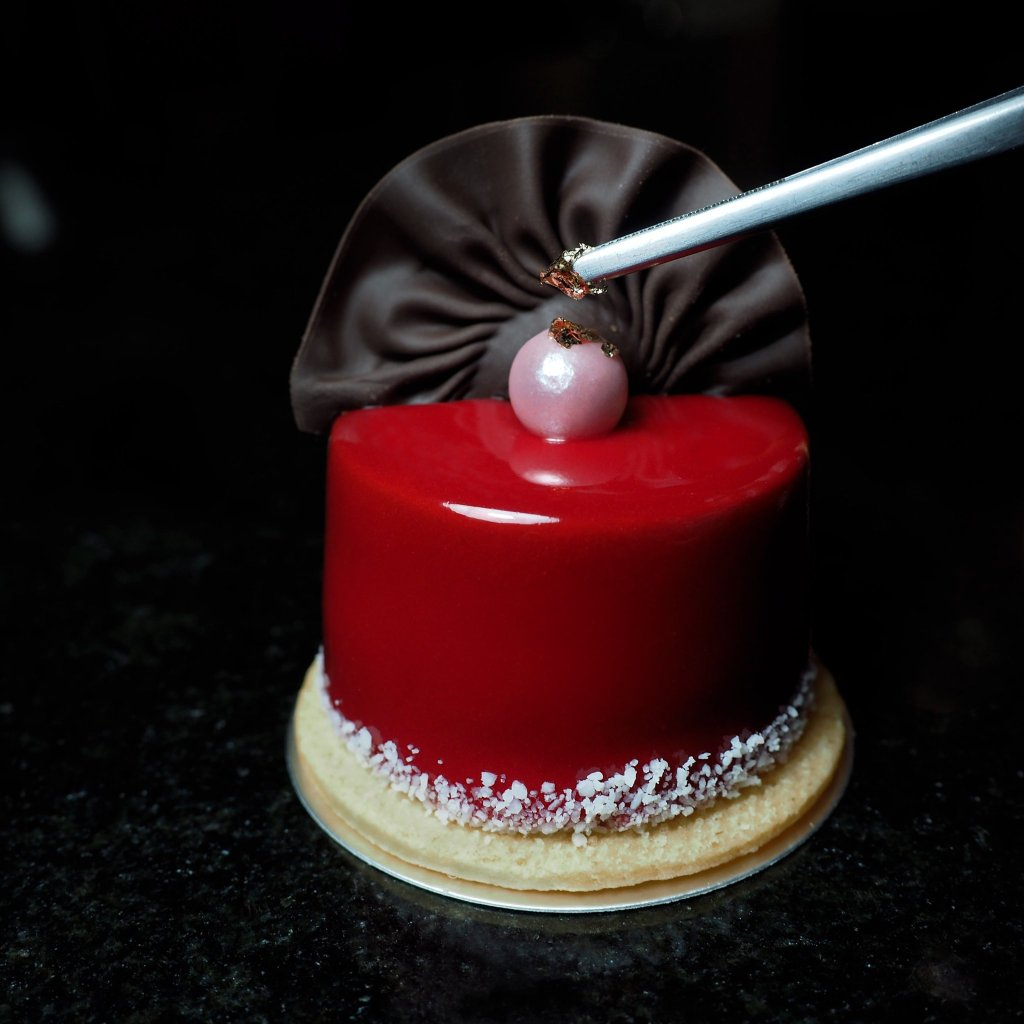 Red mirror glaze cake with chocolate decoration in professional food photography style.